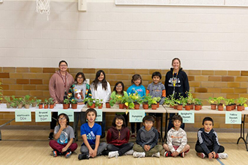 The second-grade class smiles for a photo as they open for business, selling plants to staff to learn about money management.