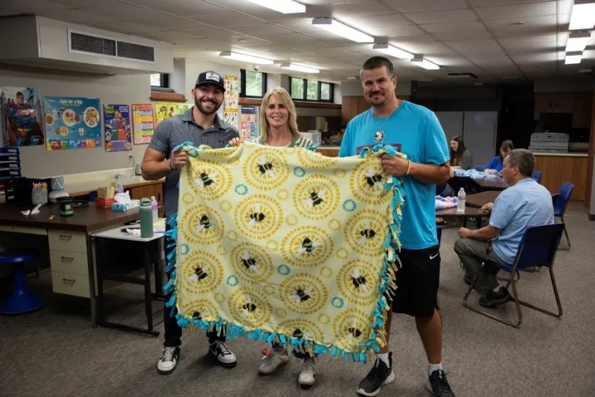 Staff members proudly hold up their completed tie blanket, knowing that someone in need will cherish it.