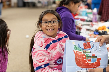 A St. Joseph’s Indian School student smiles as a volunteer hands her a wrapped present to share with her family.