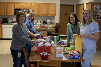 Alumni Relations and Major Gifts staff gather around tables filled with treats and self care items as they assemble more than 30 finals week care packages for St. Joseph’s alumni in college.
