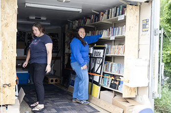 Bookmobile Intern Alexandra (right) refills the shelves with books before the Bookmobile travels throughout South Dakota.